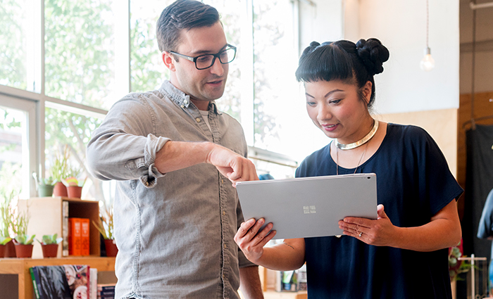 A woman holding a laptop, and a man pointing at it, trying to explain something to her, but probably not doing a great job of it.